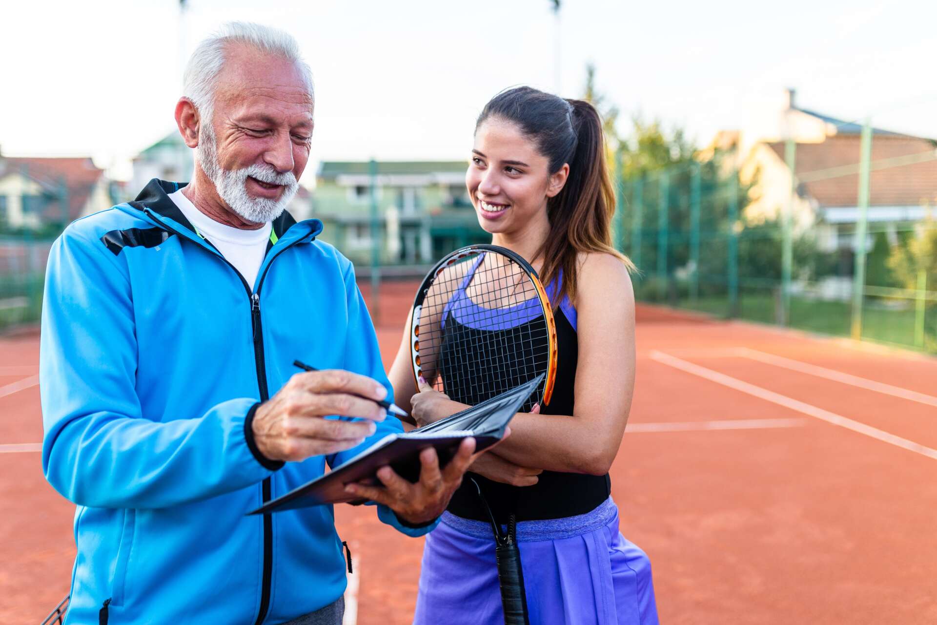 Two people at a tennis court reviewing a tennis racket and notes together