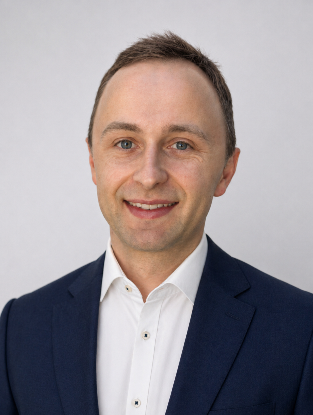 Headshot of a smiling person in a navy blazer and white shirt against a light gray background