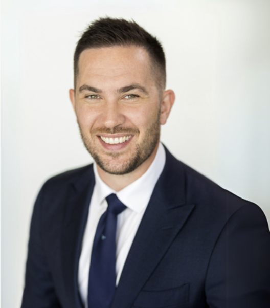Smiling man in a navy suit and tie against a light background