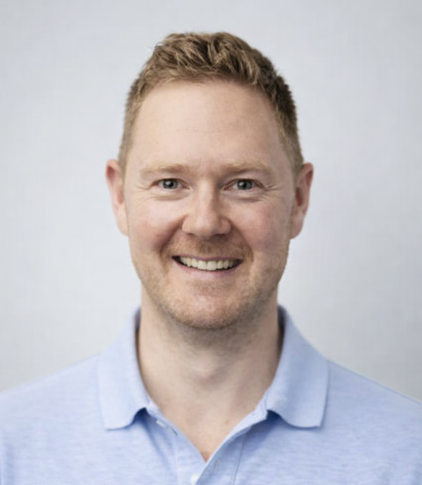 Smiling man in a light blue polo shirt against a gray background