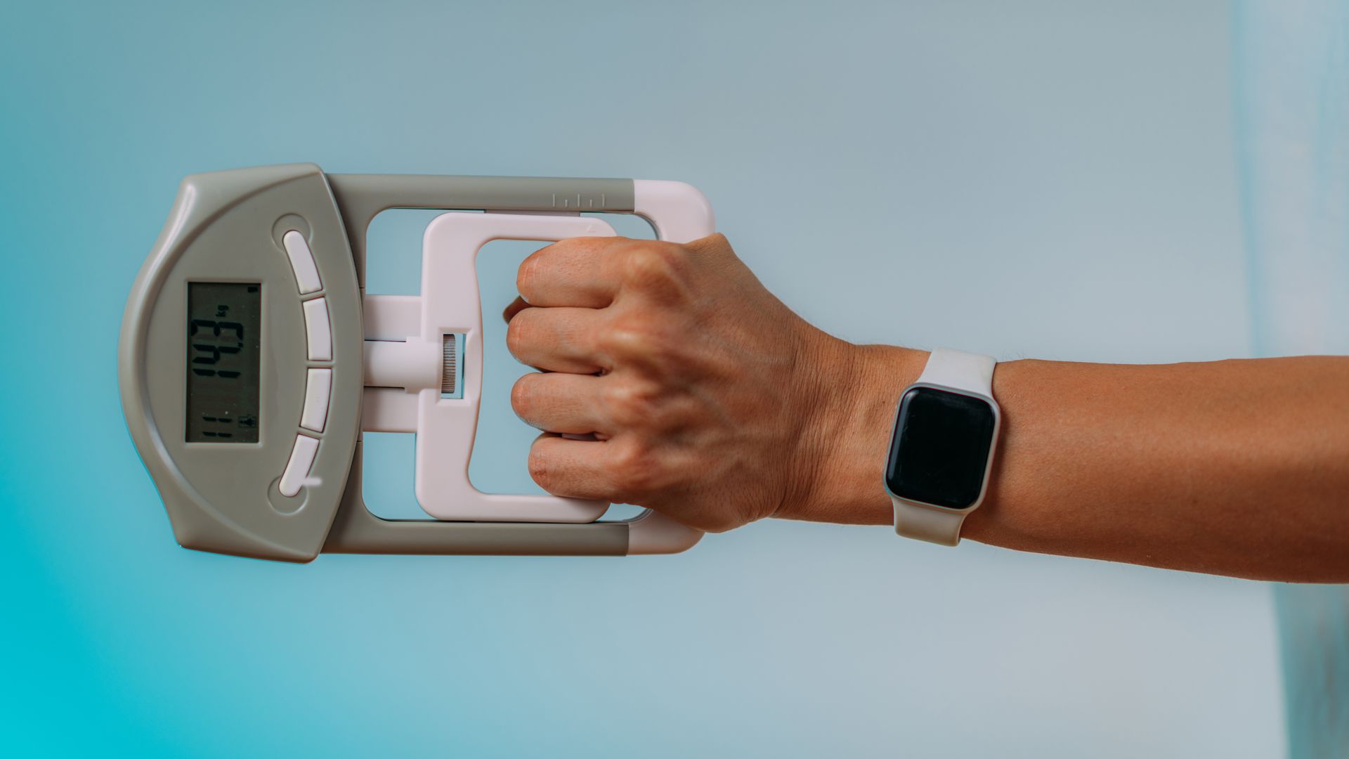 A person wearing a smart watch is holding a hand gripper for strength testing