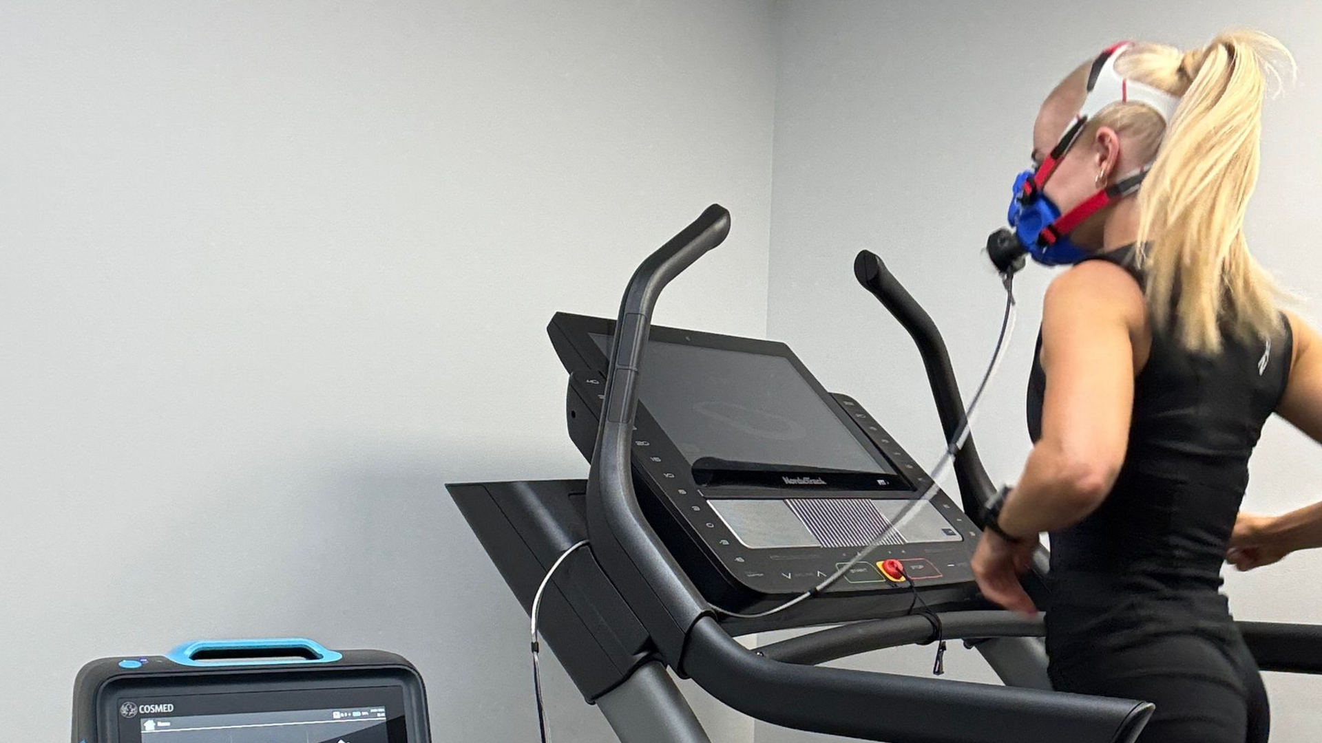 Person exercising on a treadmill while wearing a respiratory mask in a gym room.