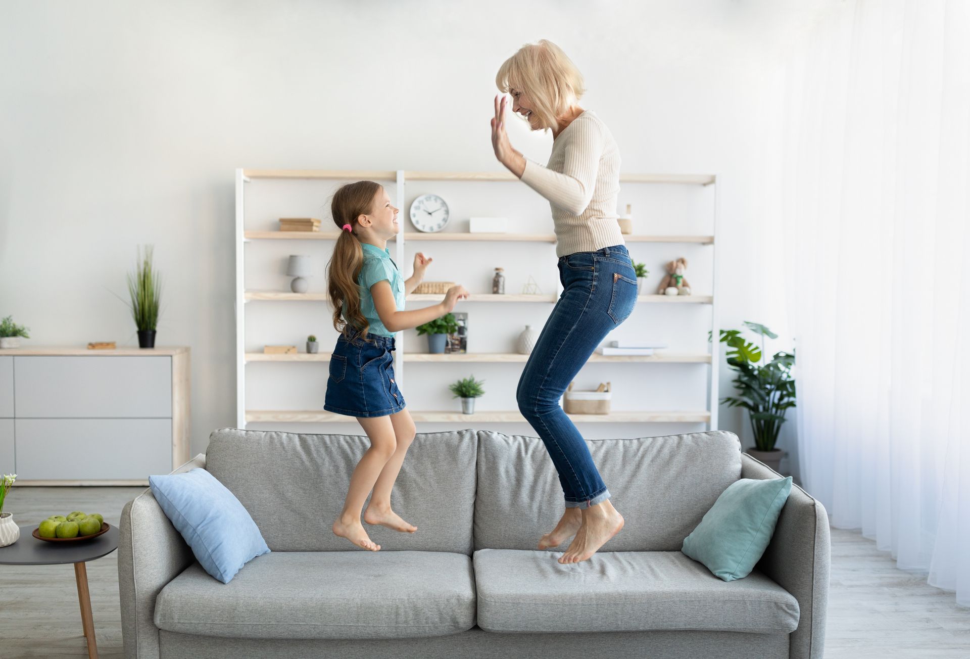 Woman and child jumping on a gray sofa in a bright living room