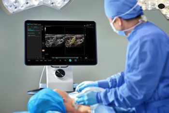 Surgeon in blue scrubs operating beside a monitor showing an ultrasound scan