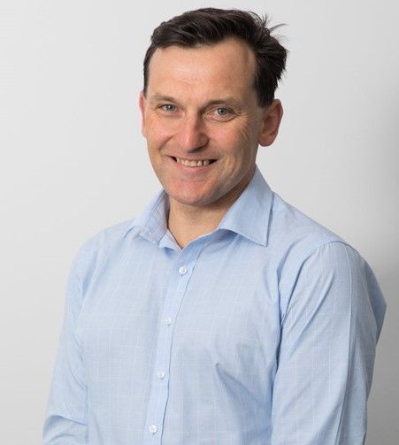 Smiling man in a light blue shirt against a plain gray background