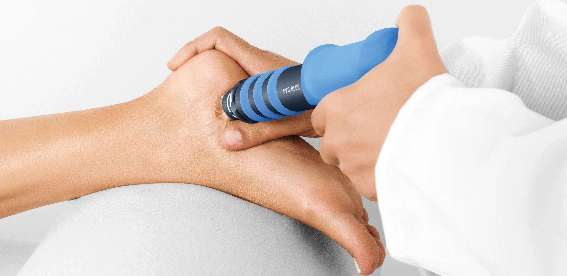 Hand holding a blue massage device against a foot on a white treatment bed