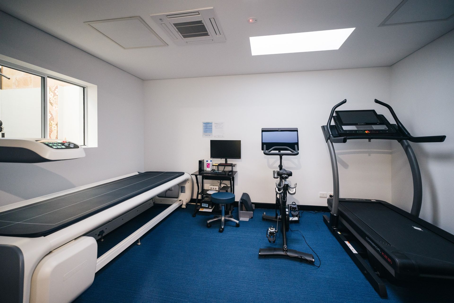A room with a DEXA scanner, treadmill and a Peloton bike in it.