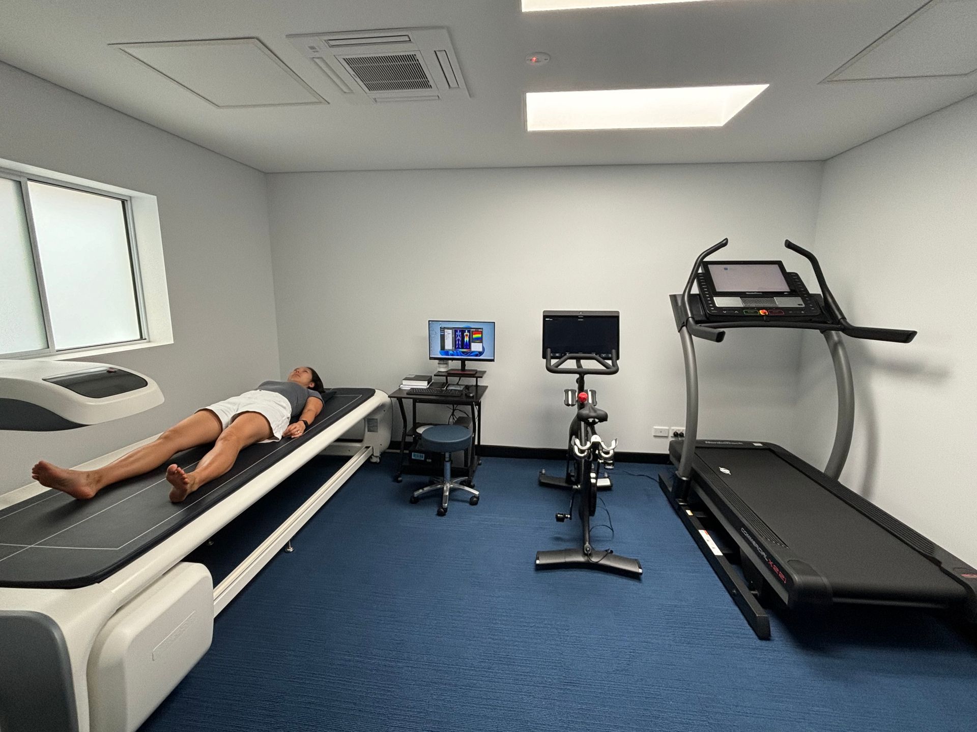A woman is laying on a bed in a room with a treadmill and a bike.