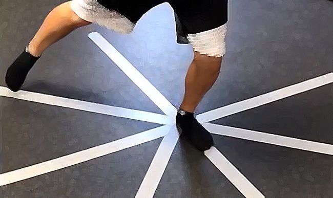 A person is standing on a black floor with white lines on it for the STAR excursion balance test