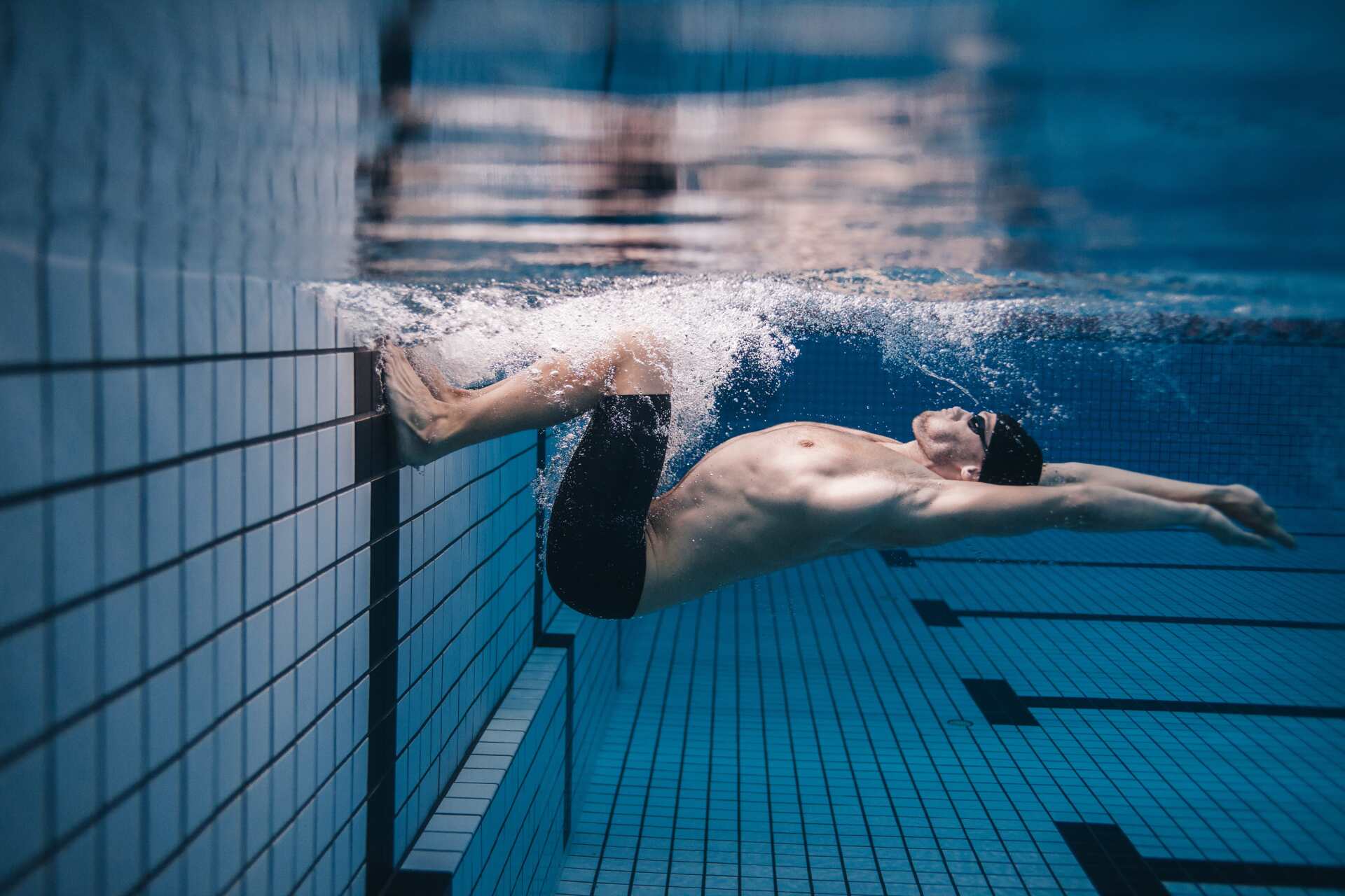 Swimmer underwater in a tiled pool, pushing off the wall in a streamlined position.