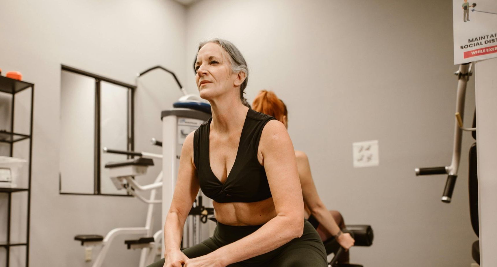 Woman exercising on a machine in a gym, wearing a black sports bra, with equipment in the background