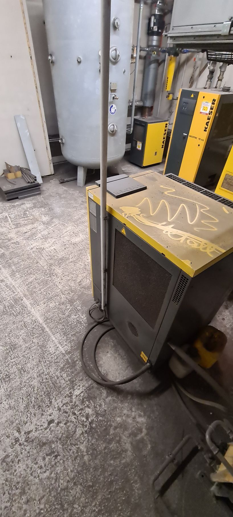 Eine Industriemaschine mit gelbem Oberteil und grauem Gehäuse in einer Werkstattumgebung.