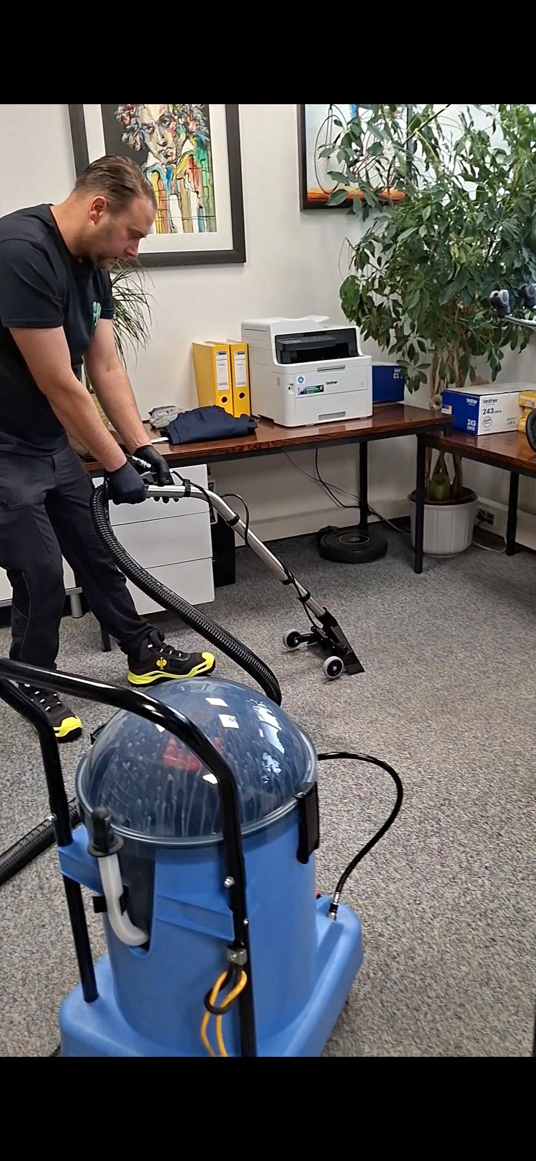 Eine Person saugt mit einem blauen Industriestaubsauger einen Teppichboden in einem Büro.
