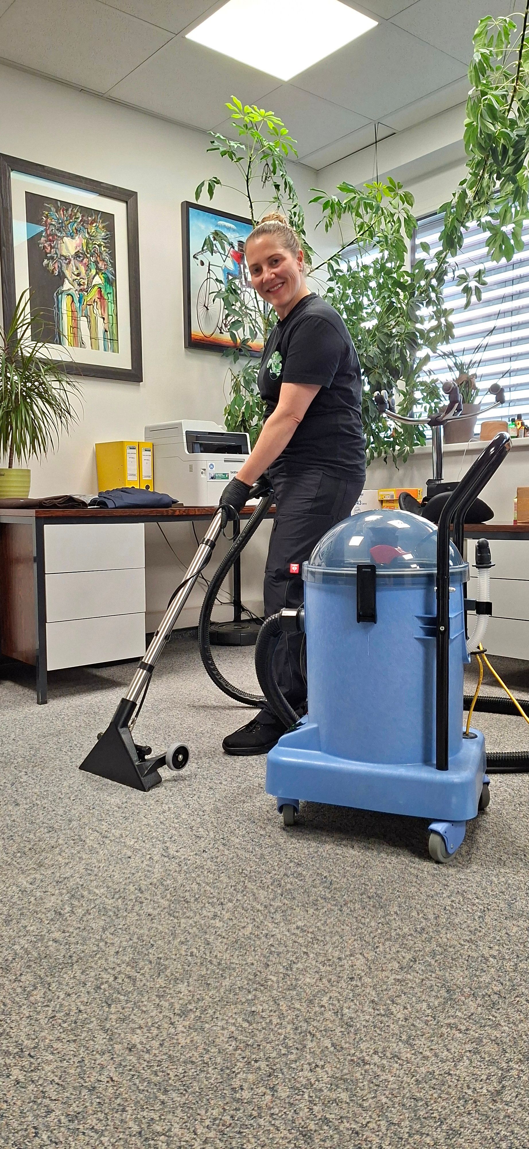 Eine Person reinigt mit einer blauen Maschine Teppiche in einem Büro. Sie lächelt und scheint die Arbeit zu genießen.