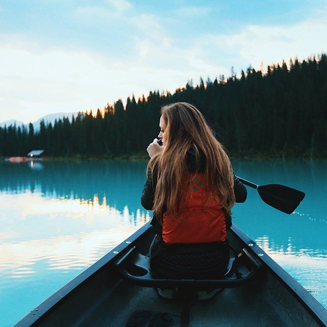 A woman in an orange vest is paddling a canoe on a lake