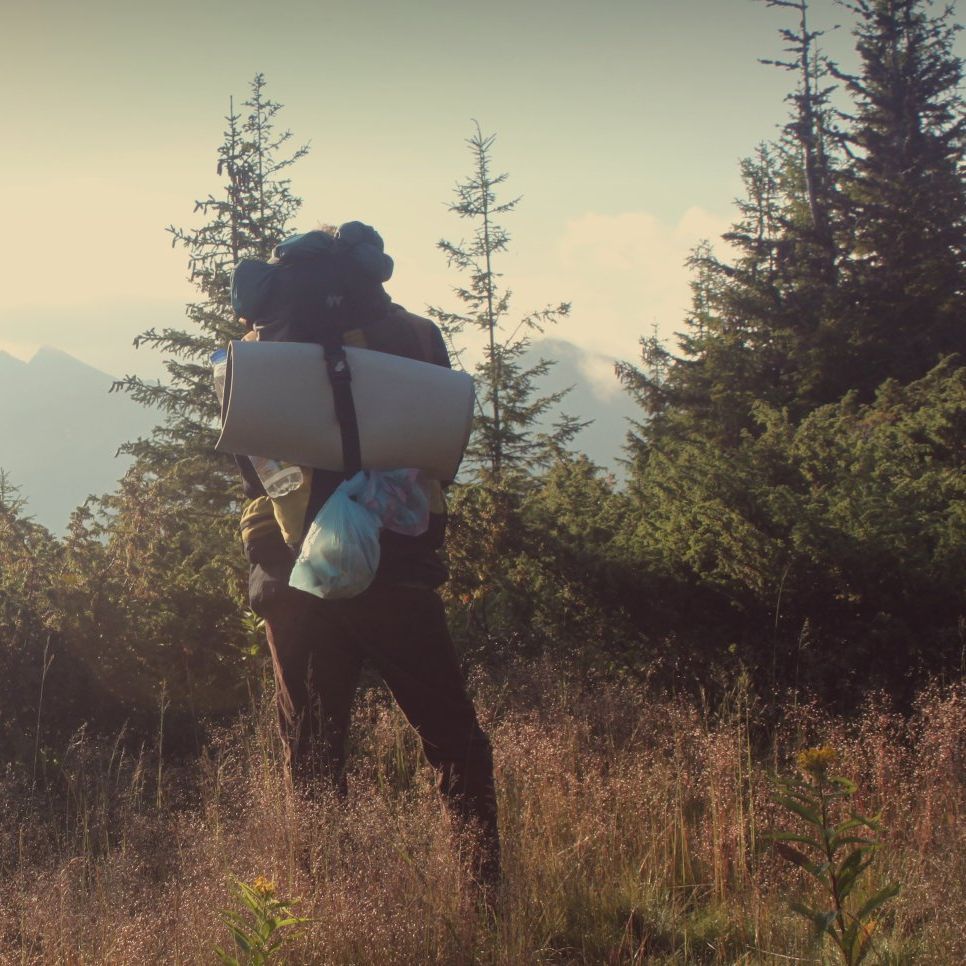 A person with a backpack and a sleeping mat on their back