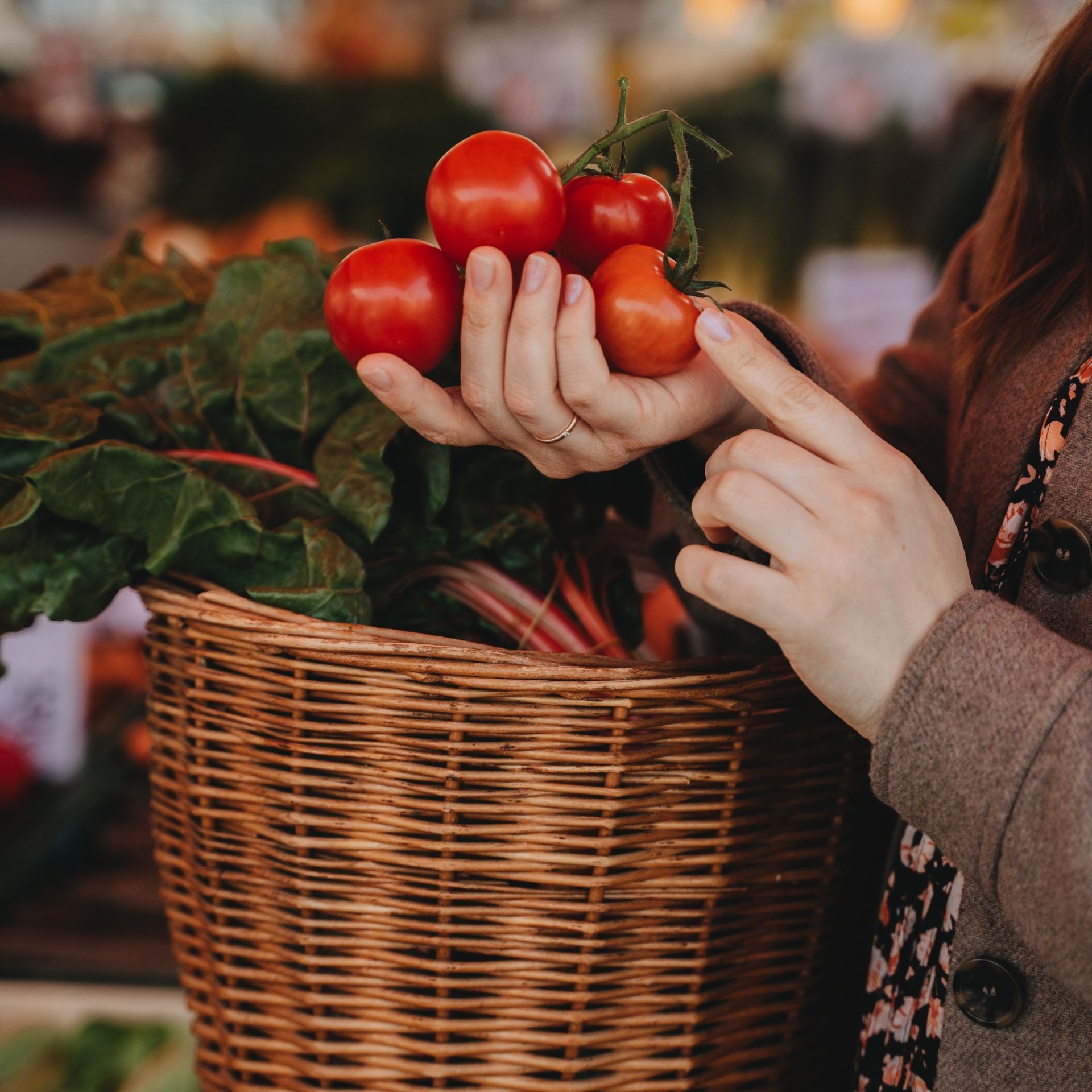 A woman is holding a basket full of vegetables including tomatoes