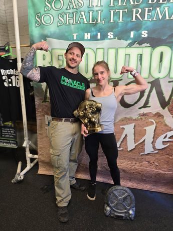 Two people pose in front of a “Revelation” event backdrop, holding a gold trophy.