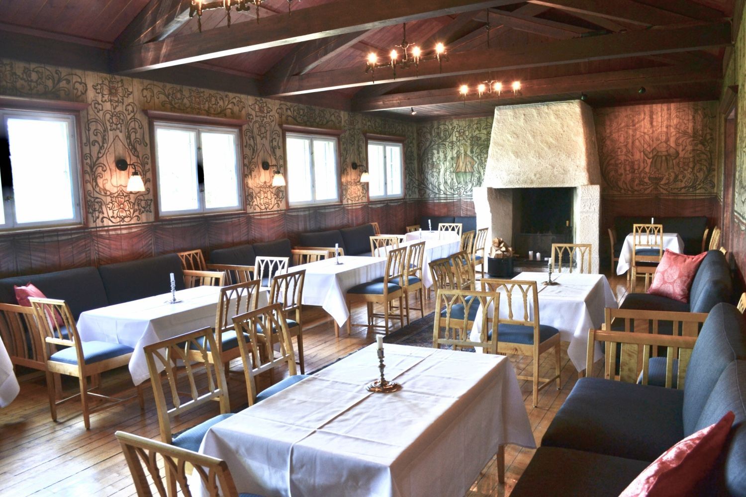 Restaurantinteriør med dekkede bord, peis, vinduer og mørk treverk.