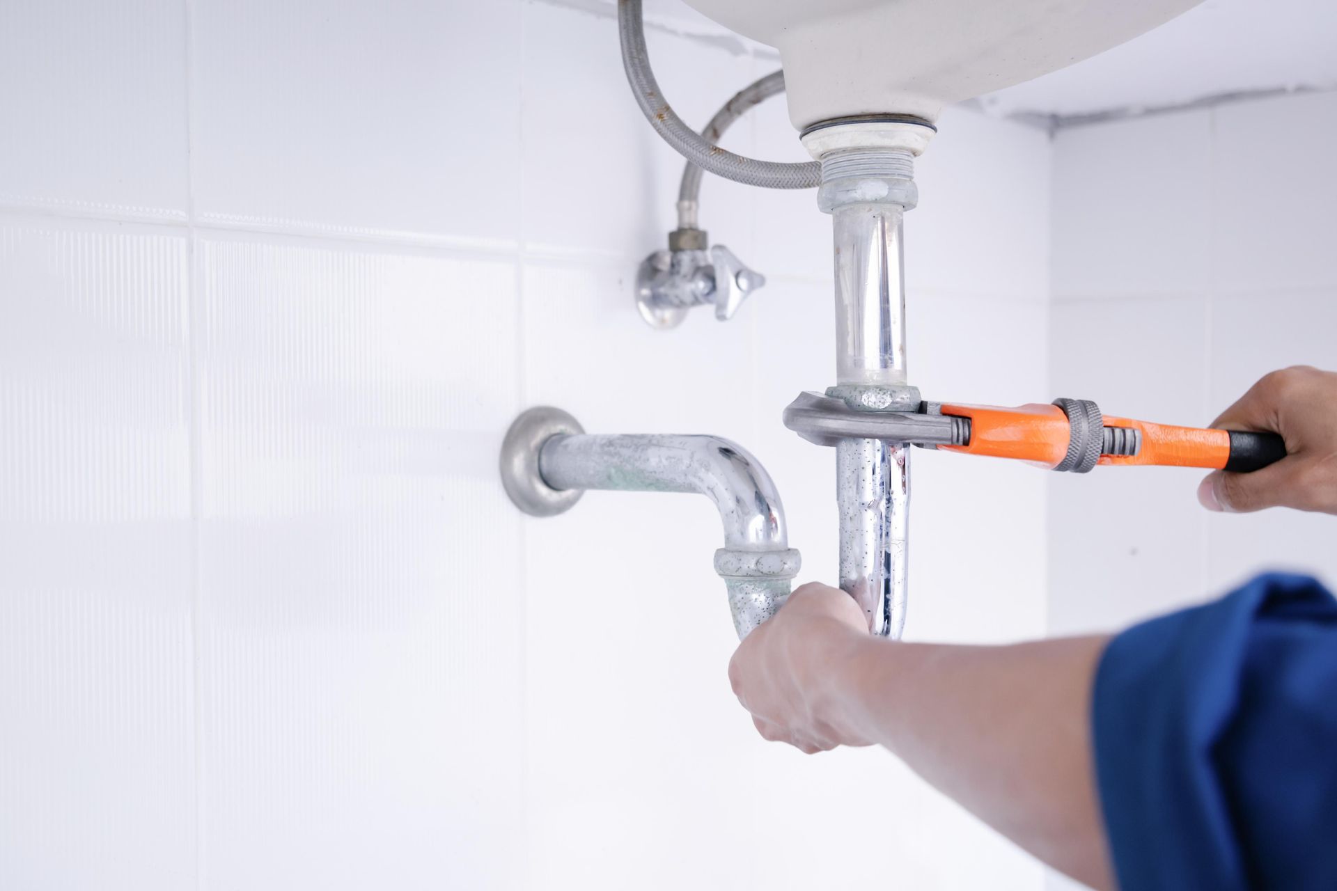 A plumber is fixing a sink pipe with a wrench.