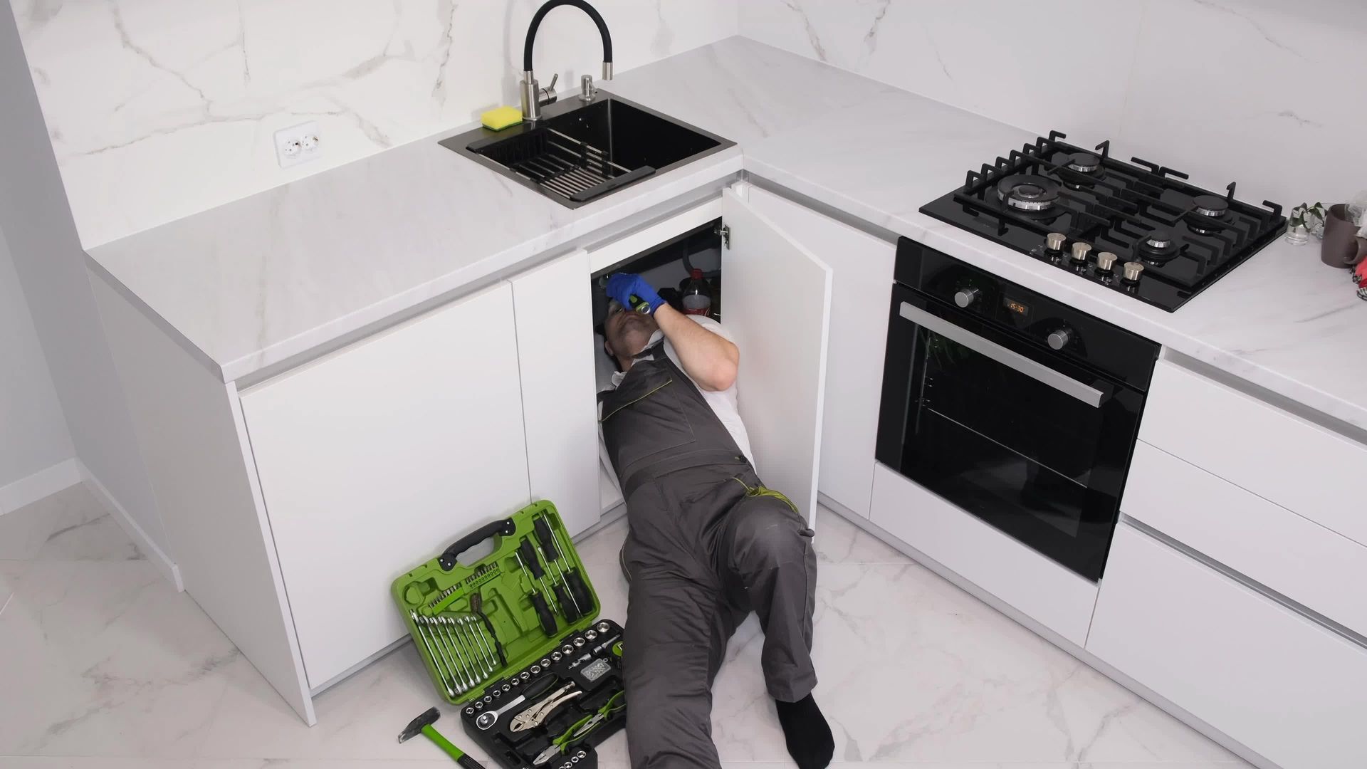A plumber is fixing a sink in a kitchen.