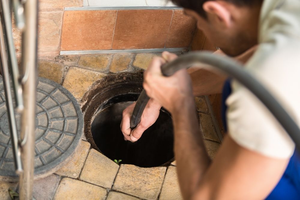 A man is cleaning a manhole with a hose.