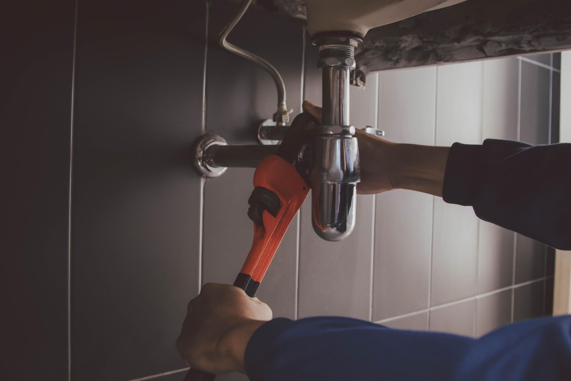 A plumber is fixing a sink with a wrench.