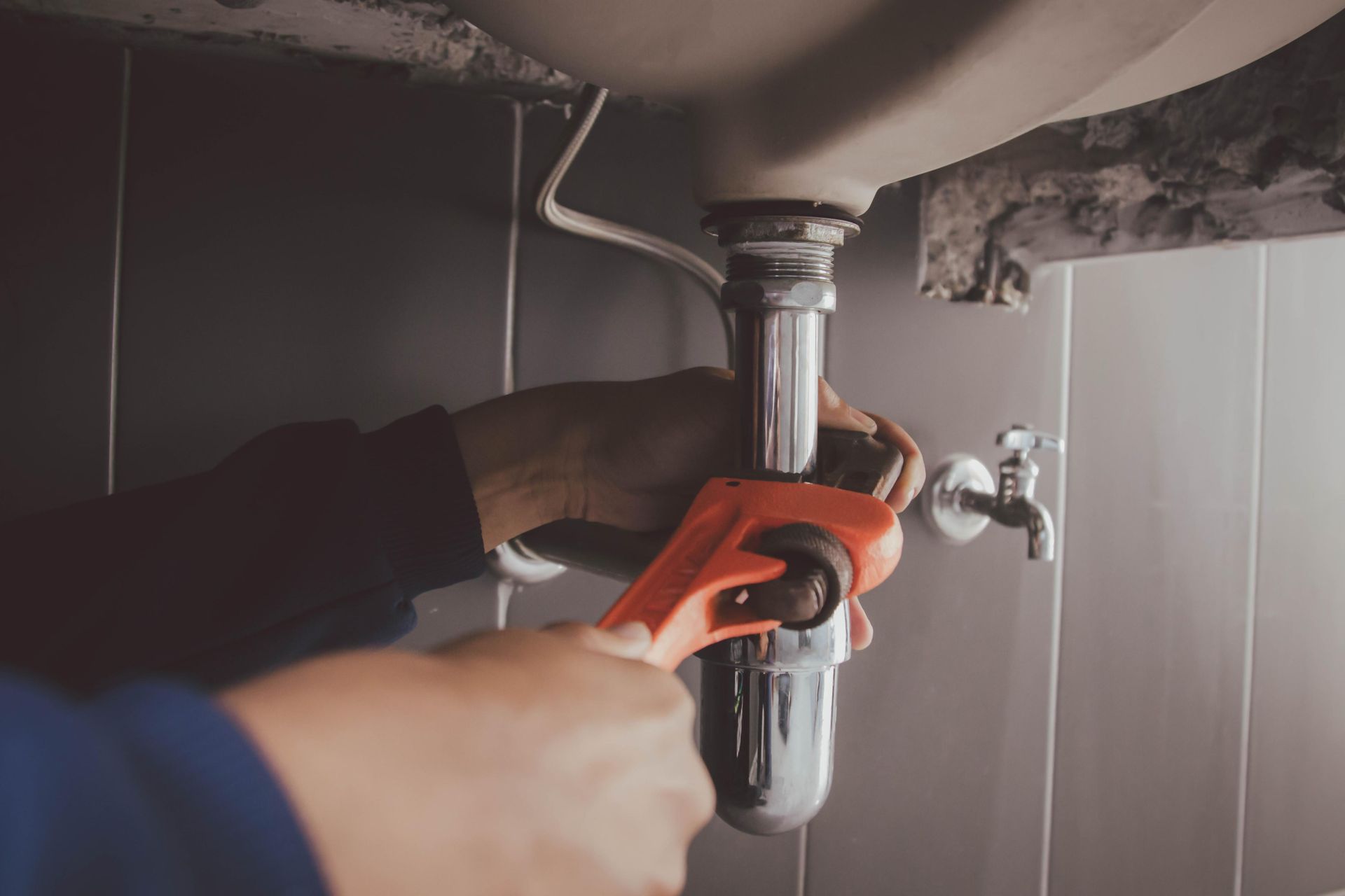 A plumber is fixing a sink pipe with a wrench.