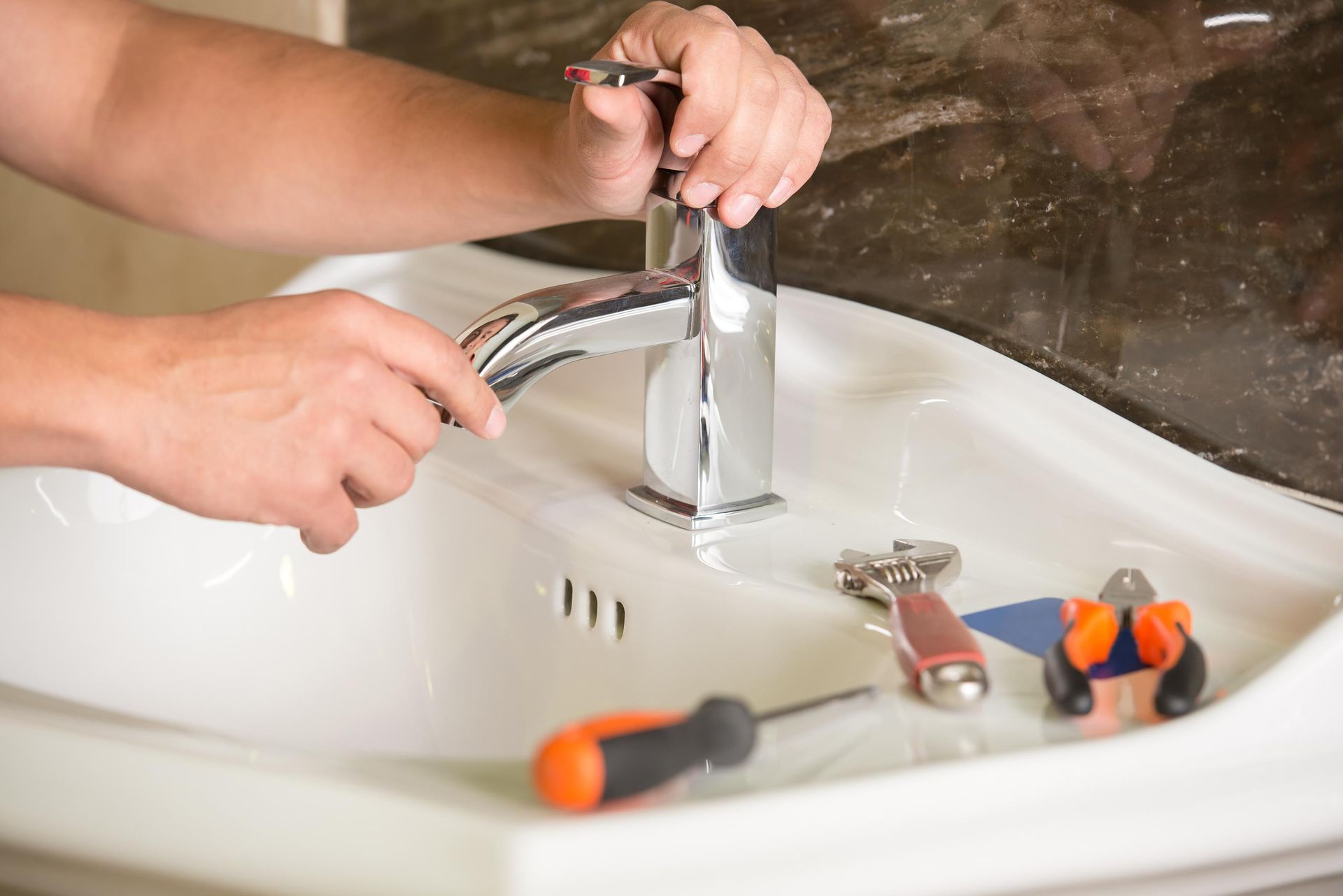 A person is fixing a faucet in a bathroom sink.