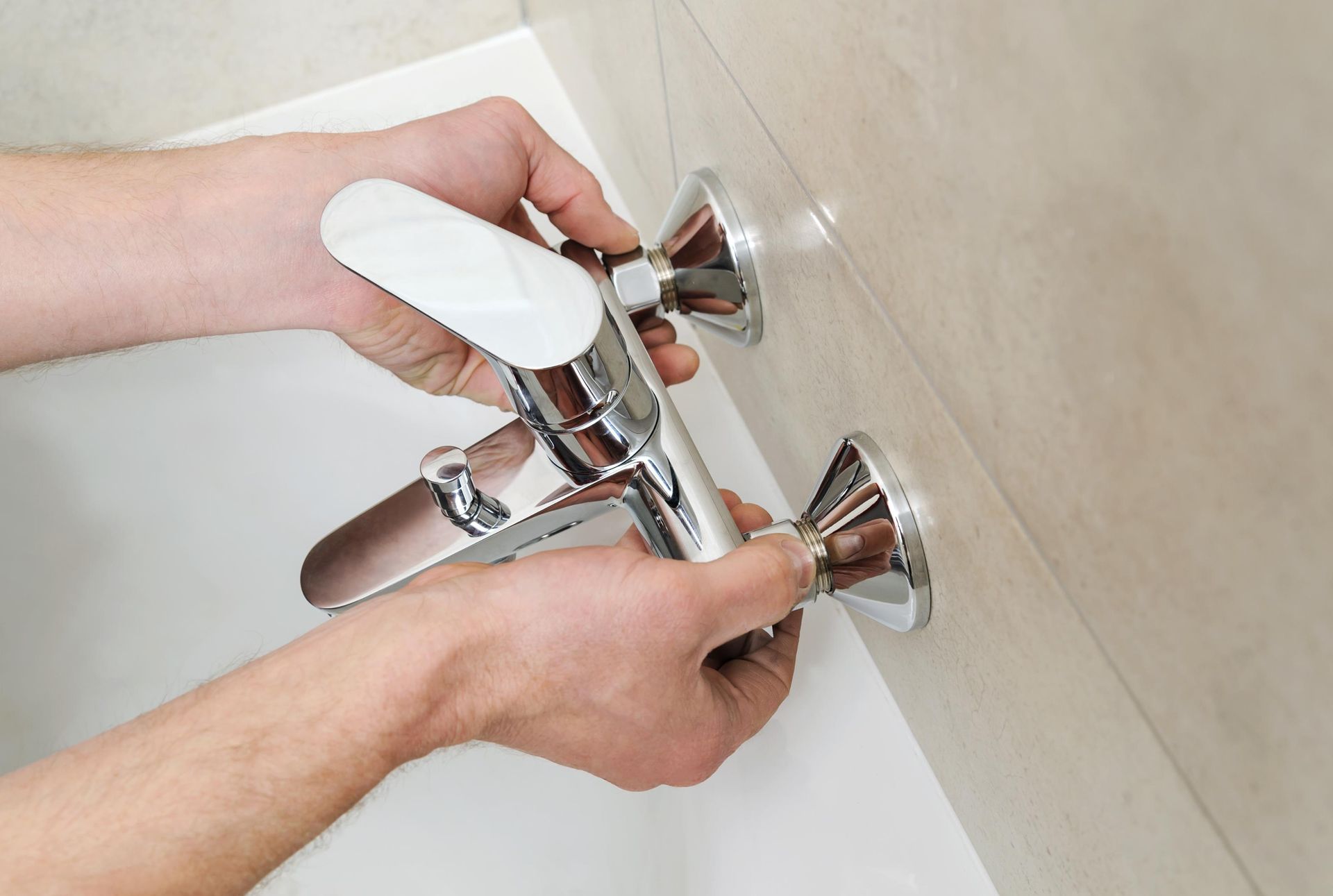 A person is fixing a bathtub faucet in a bathroom.
