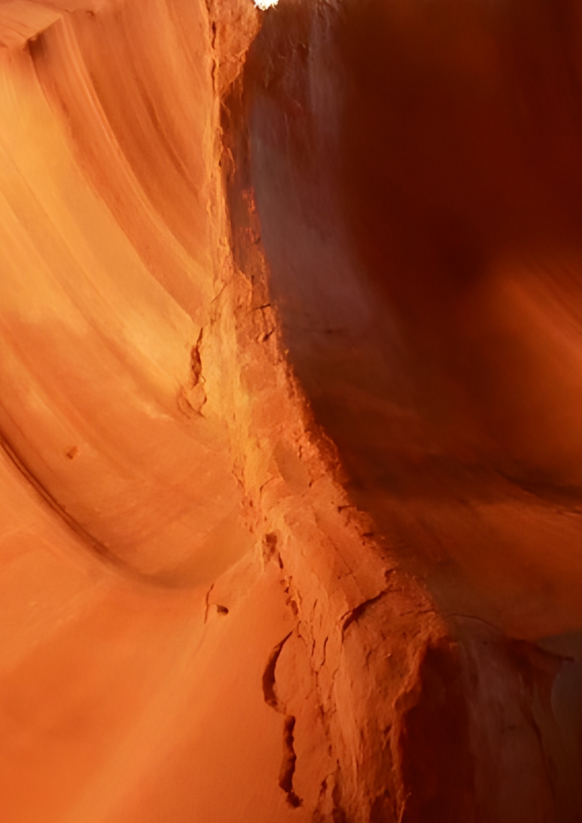 Orange sandstone canyon wall with smooth curved rock and a narrow crevice