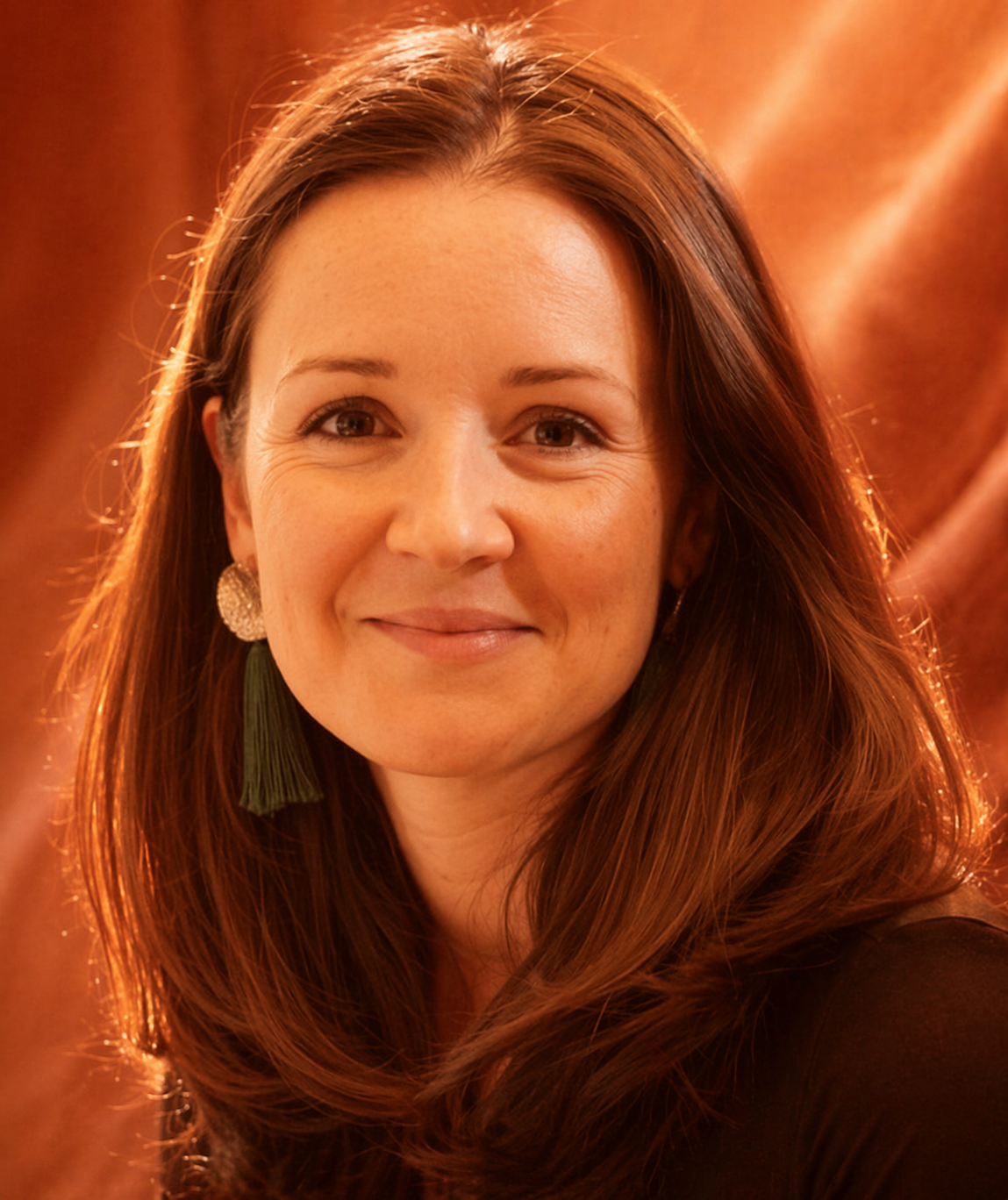 Portrait of a smiling woman with auburn hair against a warm orange background