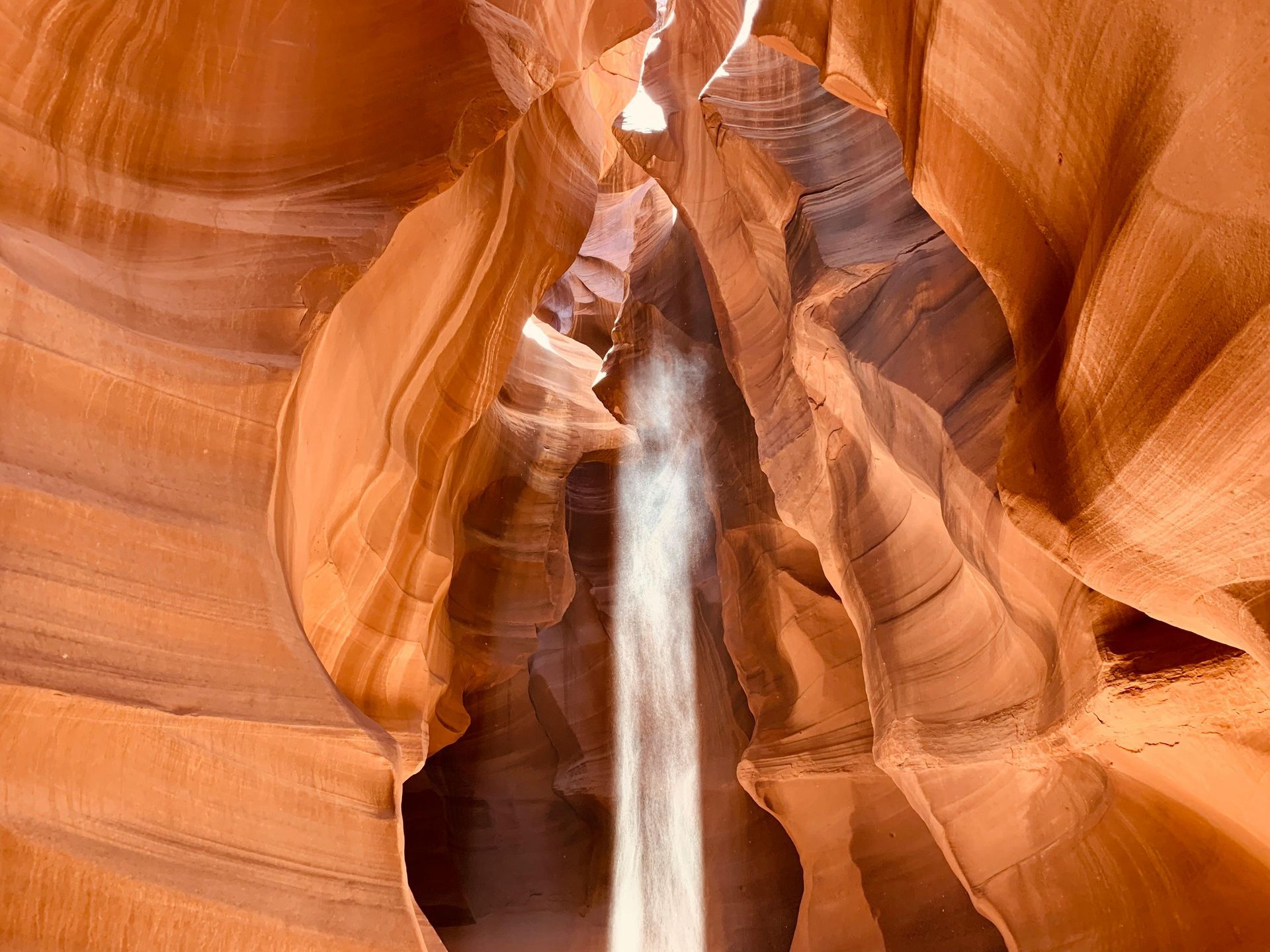 Narrow slot canyon with orange sandstone walls and a bright shaft of light inside