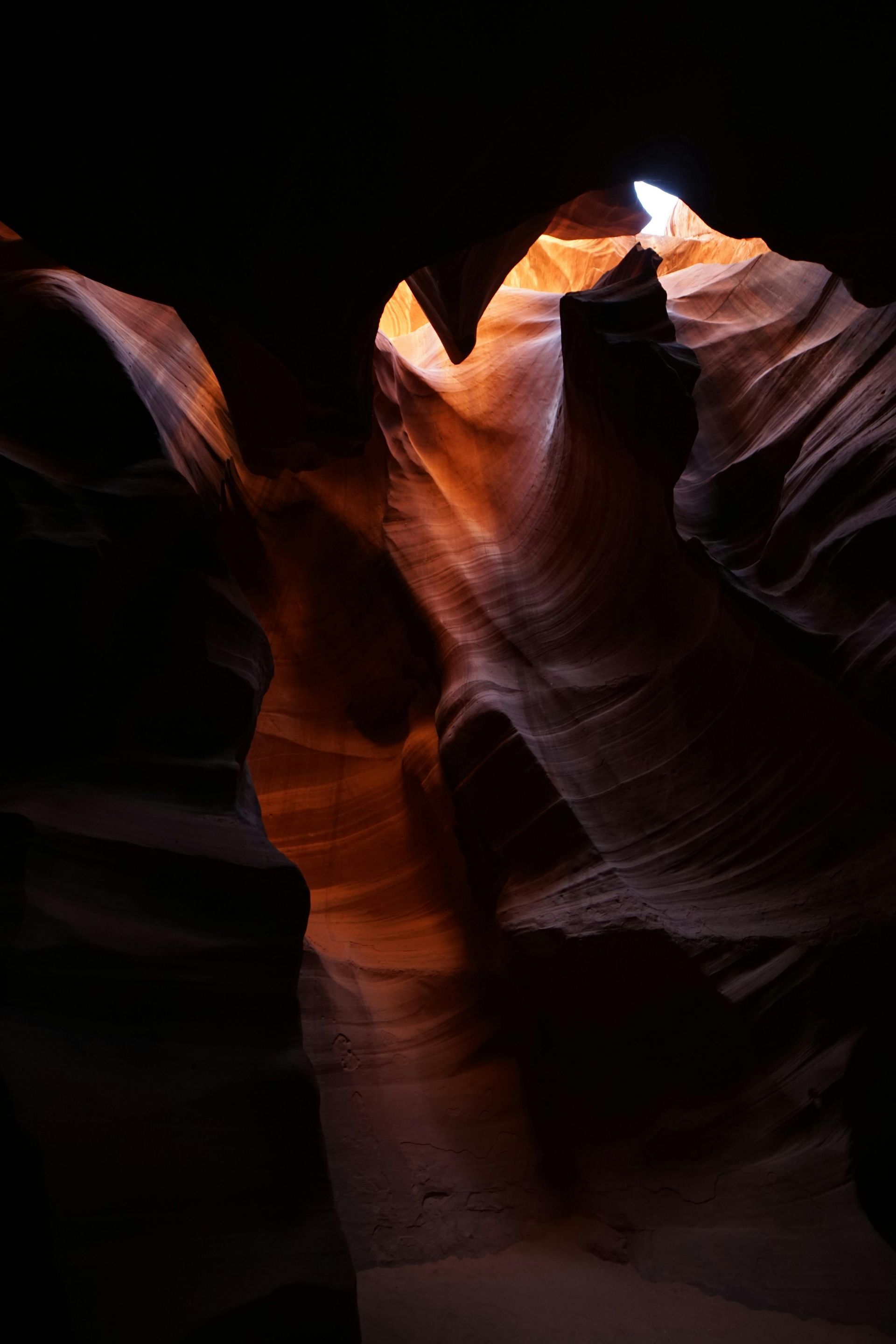 Narrow canyon with glowing orange-red sandstone walls and a bright light opening above