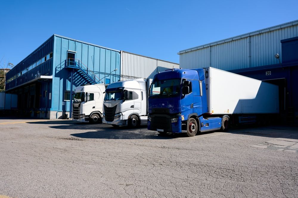 Trucks parked outside a blue warehouse on a sunny industrial lot