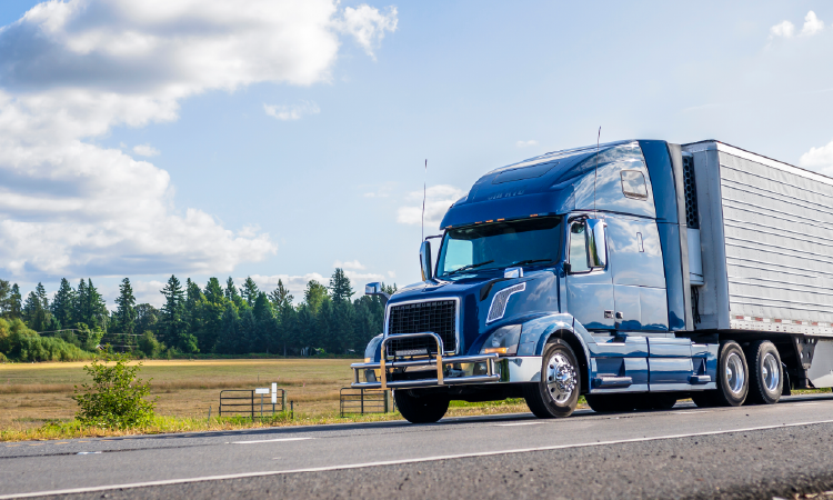 Blue refrigerated semi-truck hauling temperature-controlled freight on highway under clear sky.