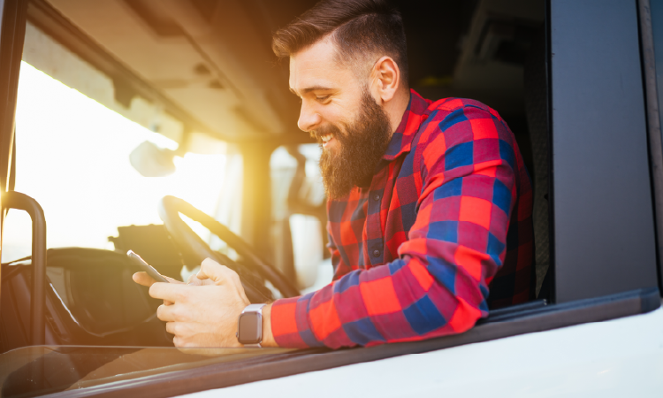 Truck driver smiling while checking shipment updates on smartphone inside refrigerated truck cab.