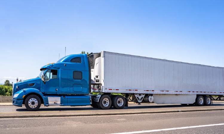 Blue refrigerated semi-truck hauling temperature-controlled freight on highway under clear sky.
