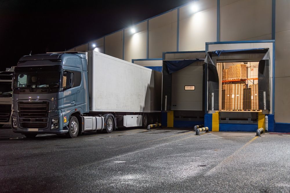 Blue semi-truck parked at a warehouse loading dock at night