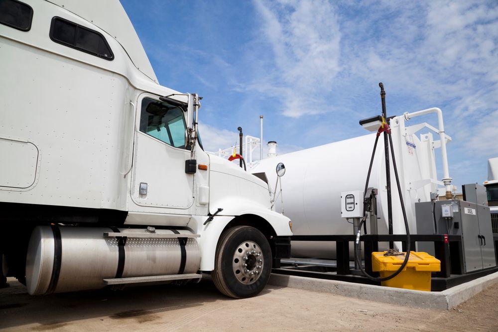White fuel tanker truck at a gas station fueling area under a blue sky