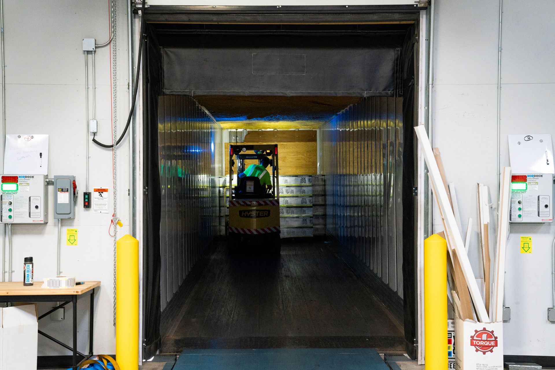 Industrial loading dock with open bay door, yellow bollards, and a forklift inside a dim warehouse tunnel.