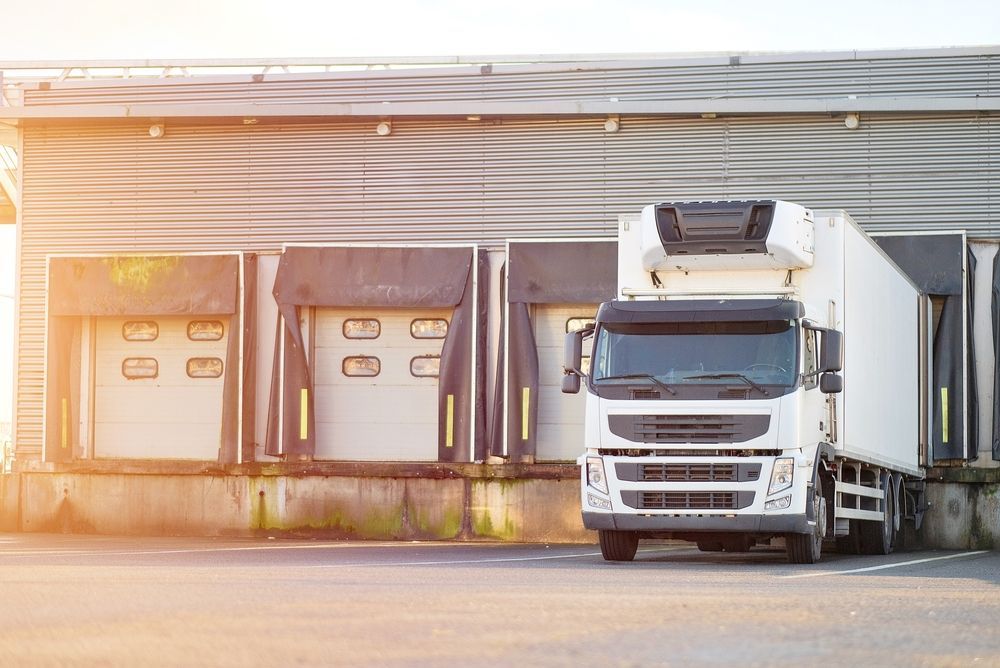 White semi-truck parked at a warehouse loading dock in front of closed bay doors
