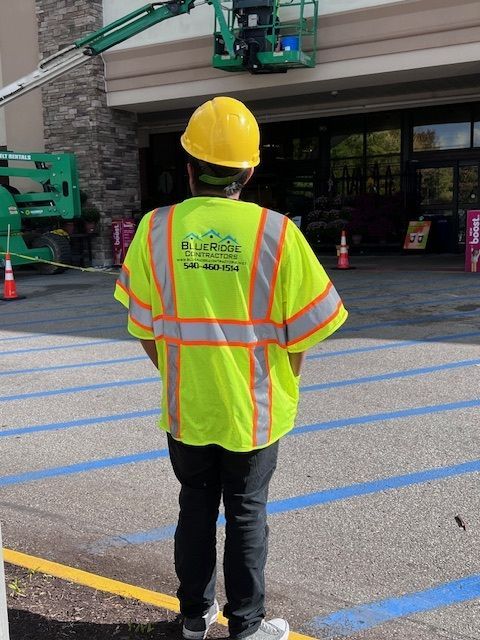 Man in safety vest and hard hat watches a lift working on a building.