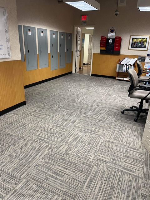 Office interior with patterned carpet, gray walls, electrical panels, and office furniture.