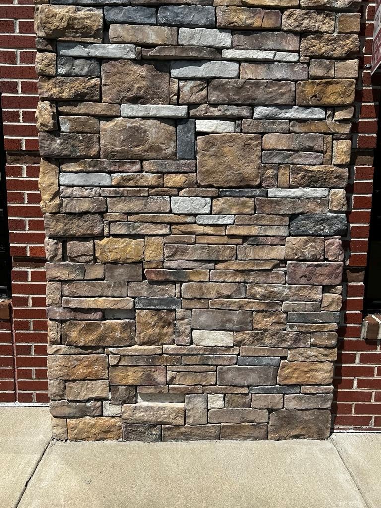 Stone veneer pillar against a brick wall, with a concrete walkway.