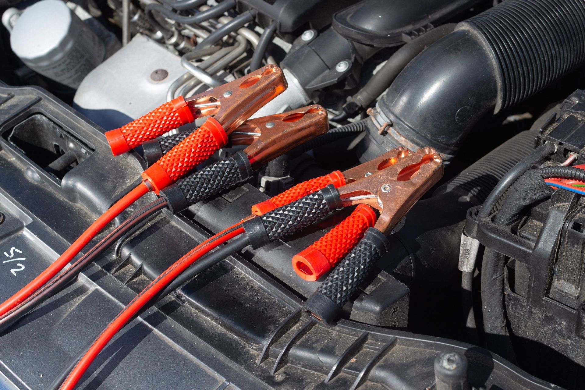 2 jumper cables sitting side by side while a technician is about to boost or jumpstart a car.