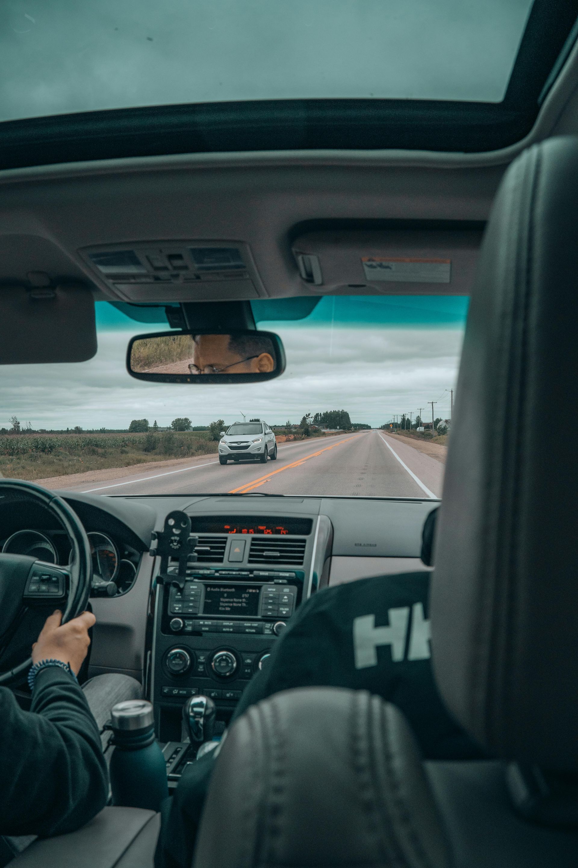 View from back seat of a car driving on a highway, with driver and front passenger visible.