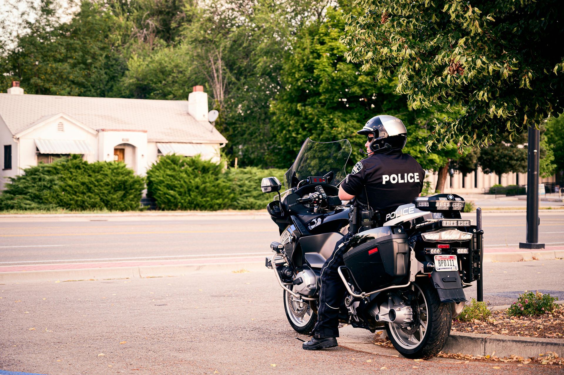 A police officer on a motorcycle parked on a street, facing away from the viewer; daytime.
