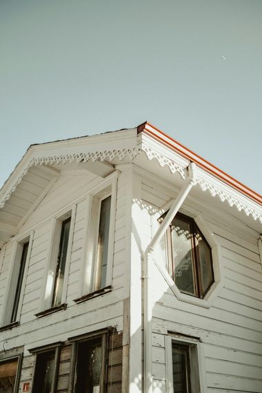 Low-angle shot of a white wooden house with decorative trim under a clear blue sky.
