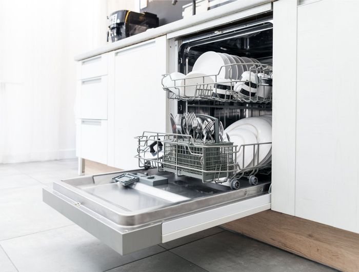 Dishwasher with open door, loaded with dishes inside white cabinets.